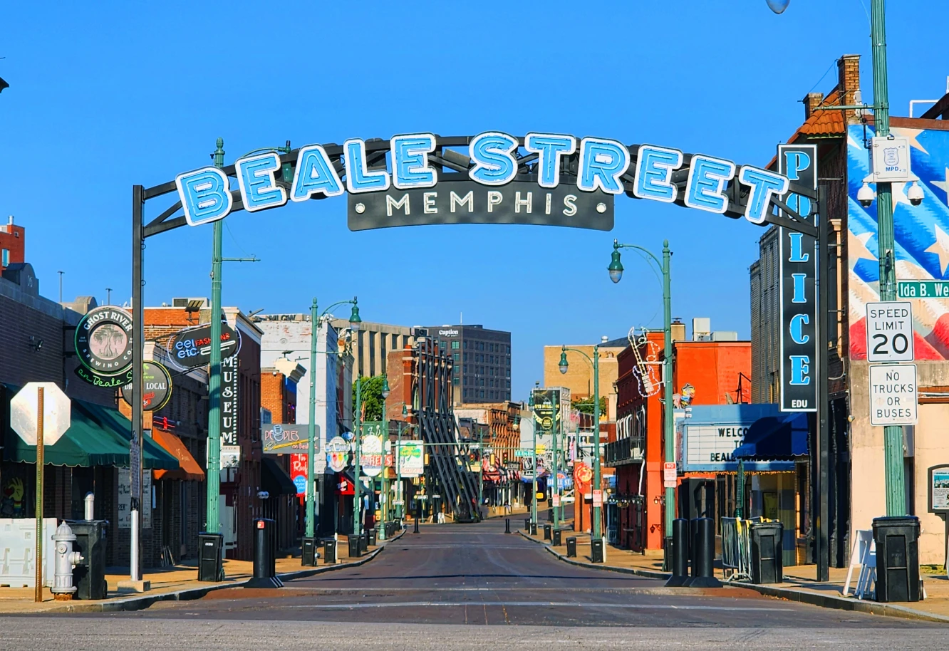Beale Street in Memphis is vibrant and empty, featuring a large overhead sign. Colorful buildings and signs line the street, creating an iconic scene.