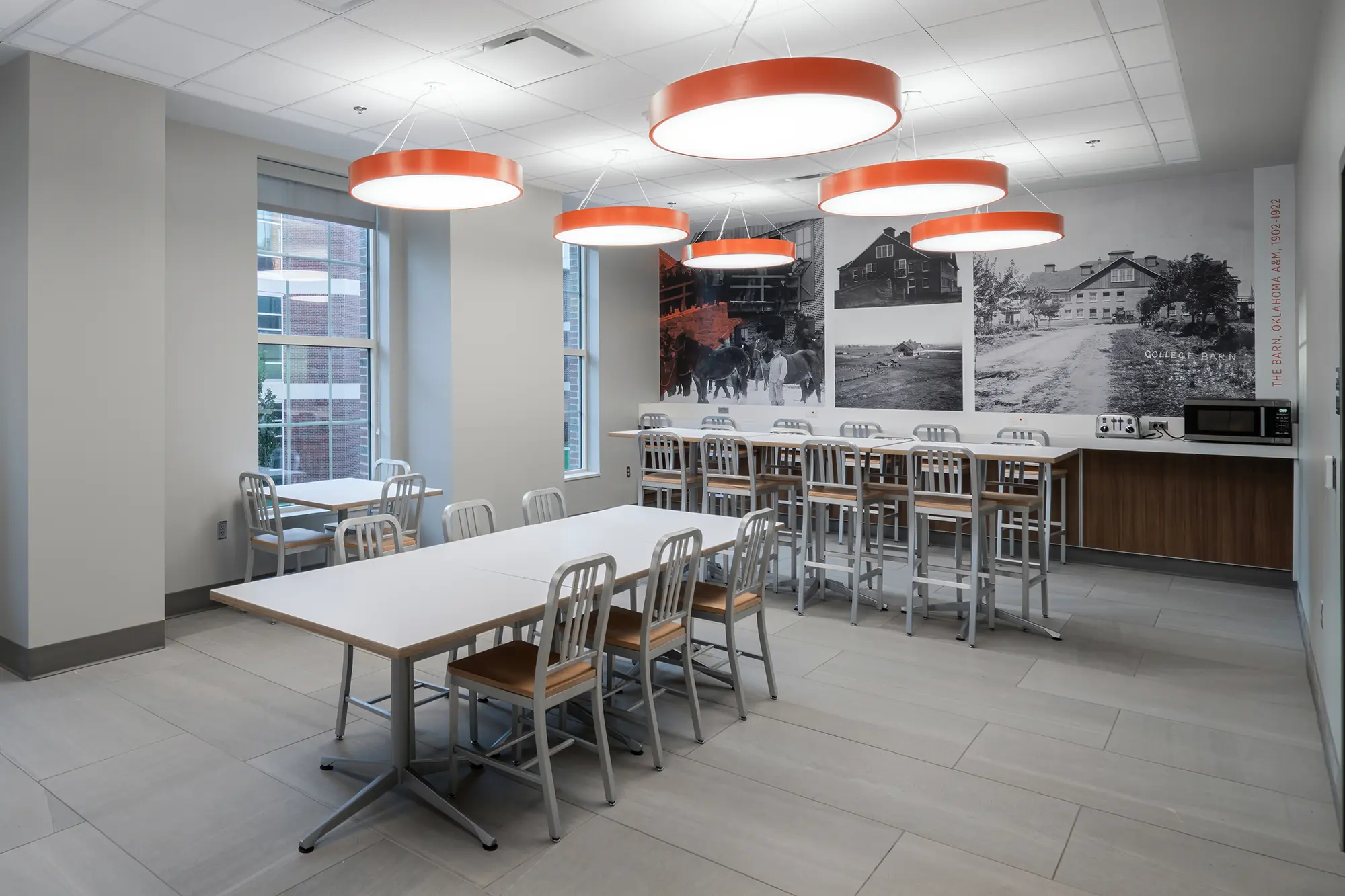 Spacious, modern break room with high ceilings, white tables, metal chairs, and large red circular lights. A black-and-white mural decorates one wall.