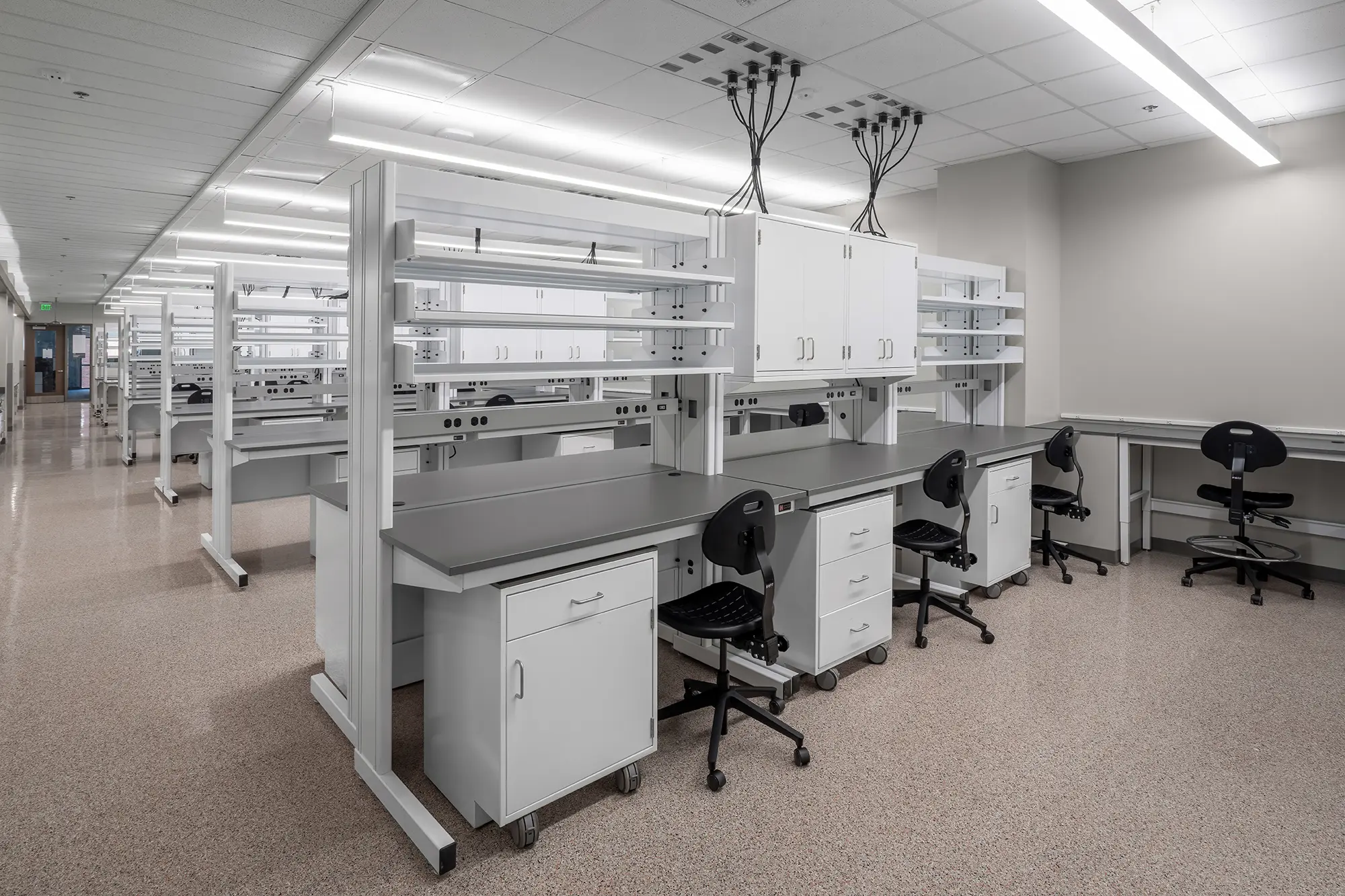 Modern laboratory with white workstations, black chairs, and overhead storage. Bright, clean, and spacious, conveying a professional atmosphere.