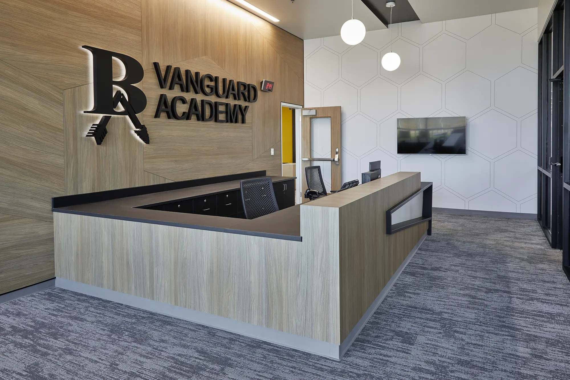 Sleek reception area at Vanguard Academy with modern wood finishes, a black counter, and geometric wall design. A welcoming, professional atmosphere.