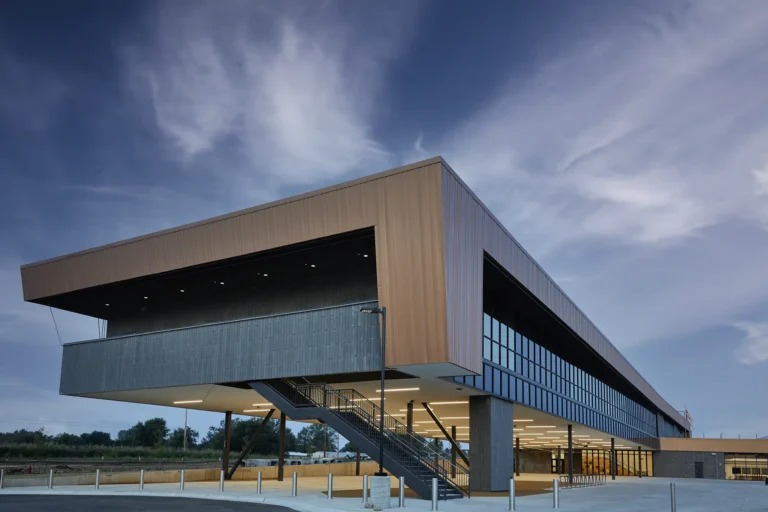 Modern two-story building with sleek design and large glass windows under a dynamic cloudy sky, evoking a sense of innovation and openness.