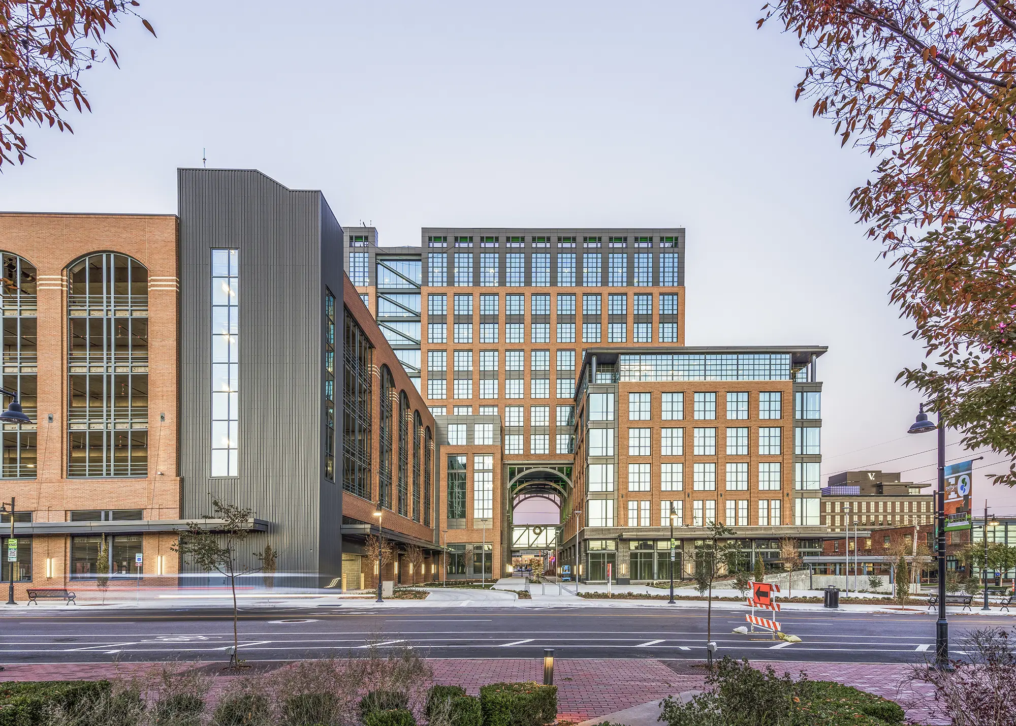 A modern building with a combination of brick, glass, and steel elements stands against a clear sky. Autumn trees frame the scene, adding warmth.