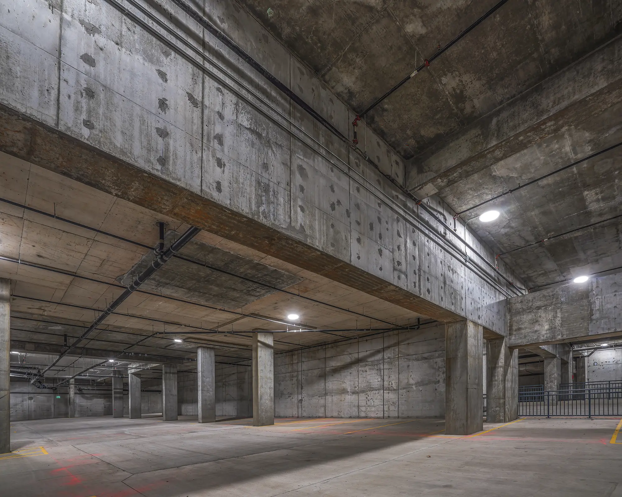 Empty underground parking garage with concrete pillars, dim lighting, and high ceilings. The space appears industrial, clean, and deserted.