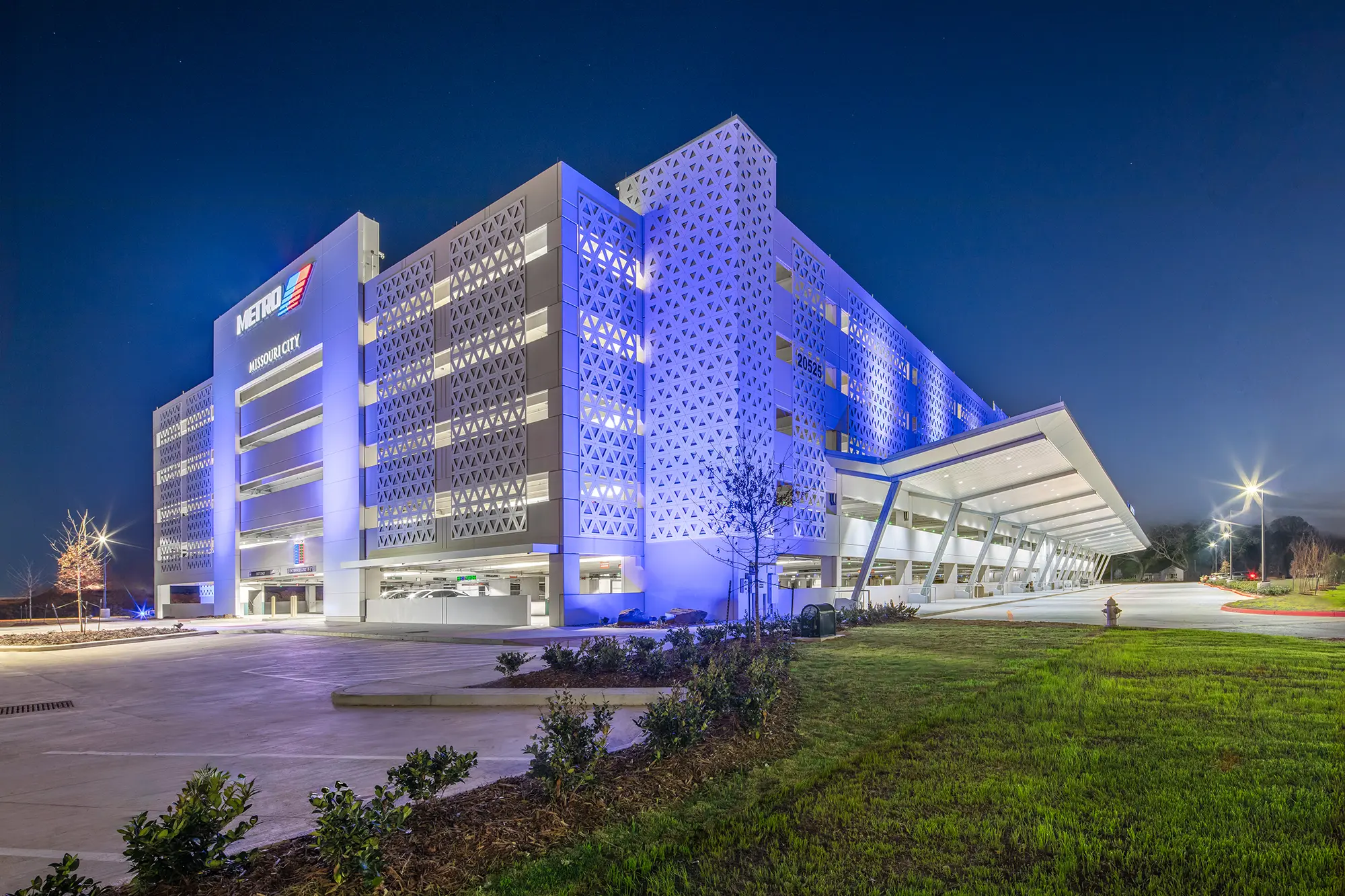 Modern multilevel parking garage illuminated with blue lights at night. Architectural patterns and illuminated entrance create a sleek, futuristic feel.