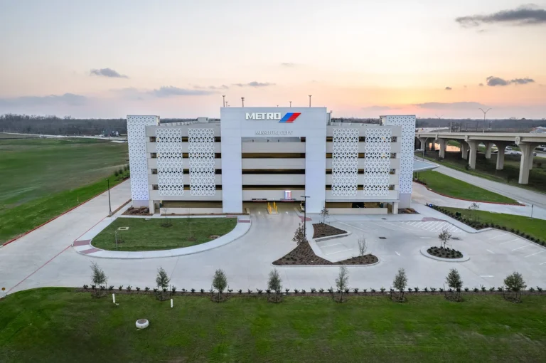 Aerial view of a modern, multi-level parking garage with METRO signage at sunset. The foreground features a neat driveway and landscaped greenery.