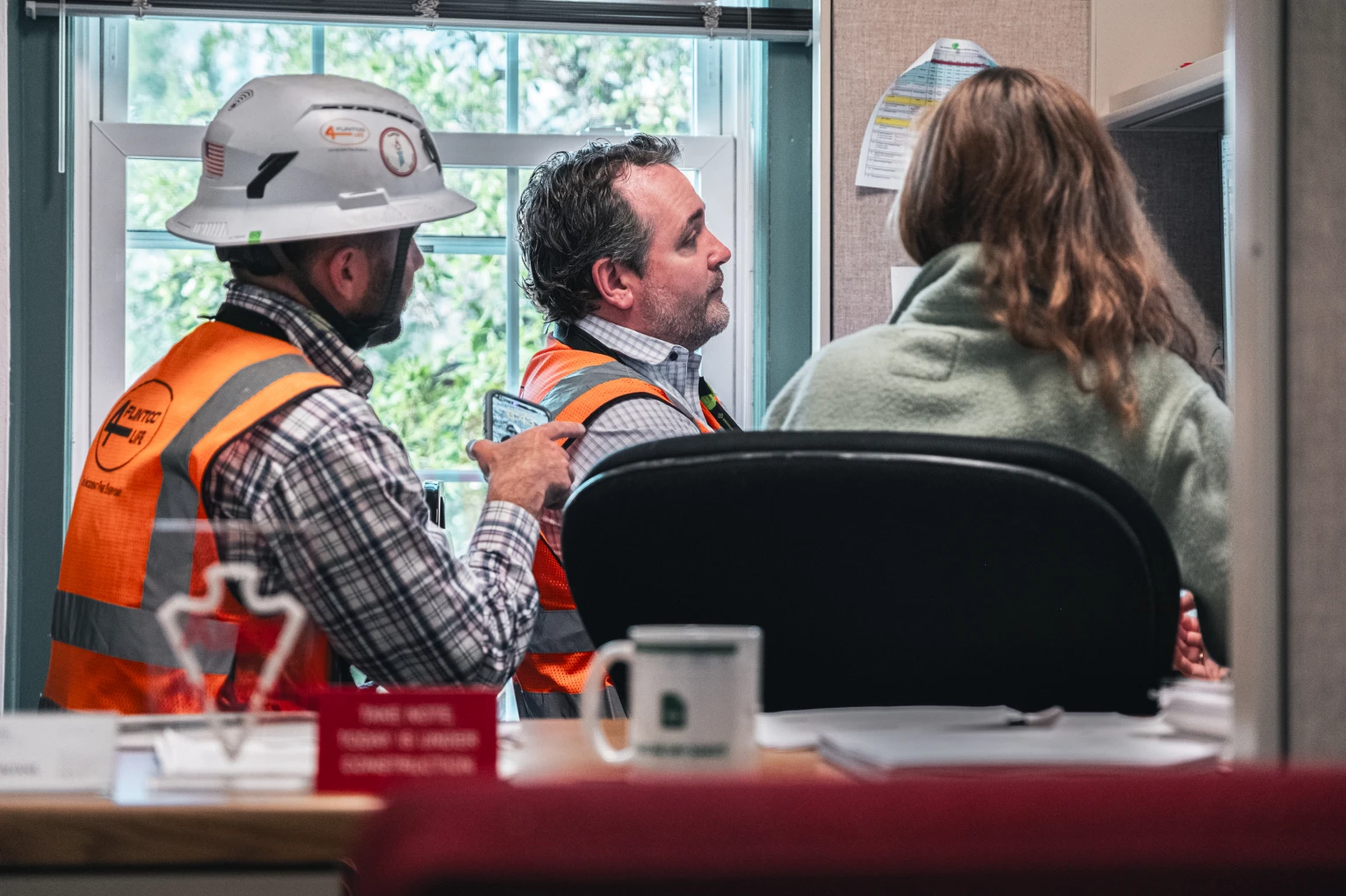 A large group of people, mostly wearing black shirts, pose together smiling in front of a rustic stone and wood building on a grassy area. It conveys a sense of camaraderie.