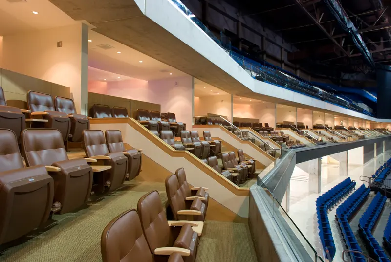 Luxurious stadium suite with rows of plush brown leather seats overlooking an arena. The setting is spacious and well-lit, conveying exclusivity.