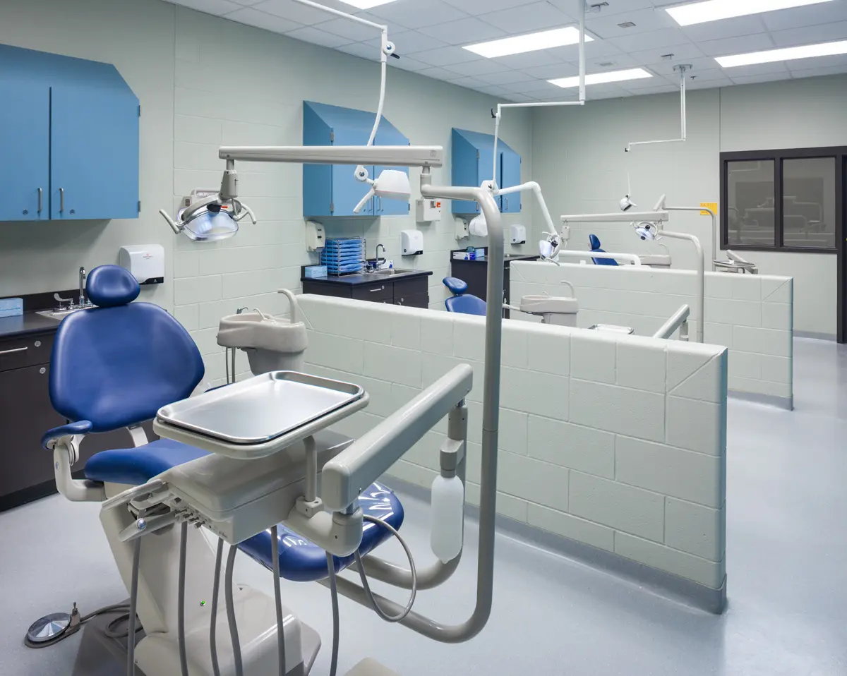 Dental clinic with modern blue chairs, white walls, and equipment. Individual workstations separated by low partitions convey a clean, clinical setting.