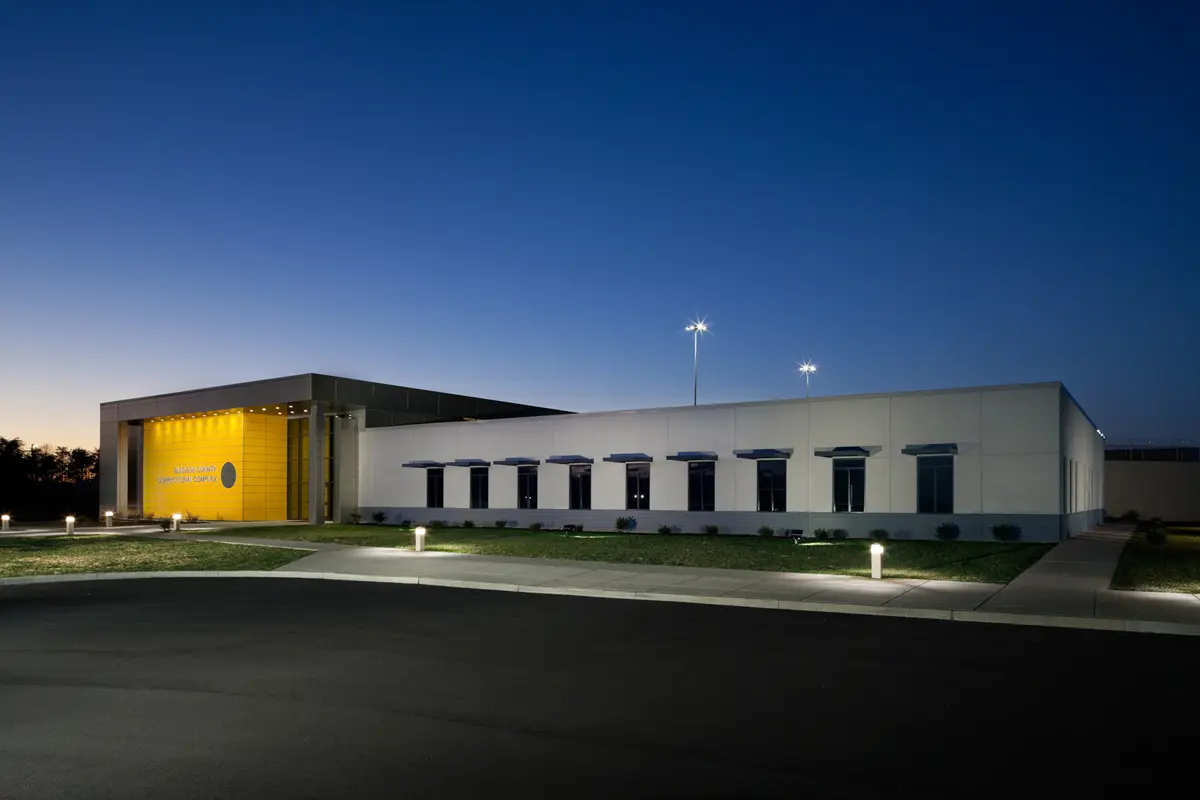 Modern building at dusk with a yellow-lit entrance and sleek design, surrounded by green lawn and glowing path lights under a clear sky.