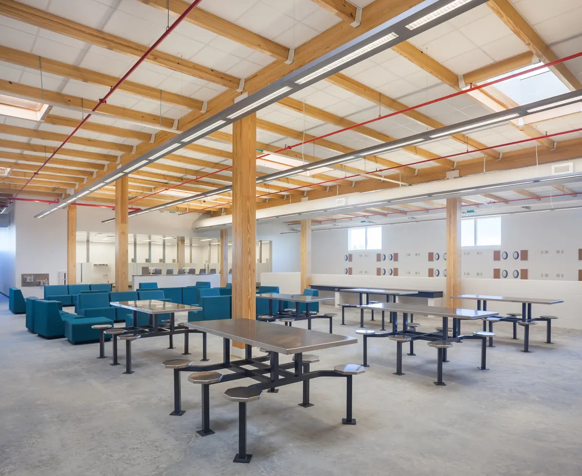 Spacious room with wooden beams and high ceiling, featuring modern blue couches and metal tables with attached stools, creating a clean, open feel.