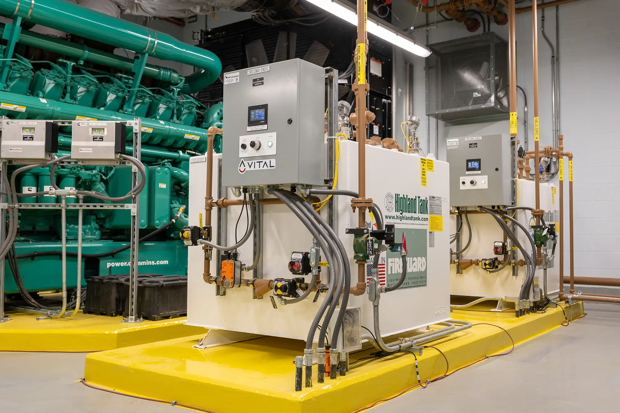 Industrial setting with two large white control panels labeled "Vital" and "Highland Tank" on yellow platforms. Green machinery is visible in the background.