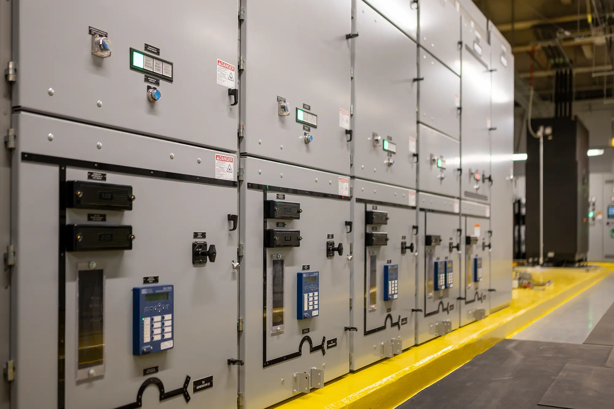 A row of industrial electrical control panels with digital displays and switches in a well-lit facility, conveying a sense of precision and efficiency.