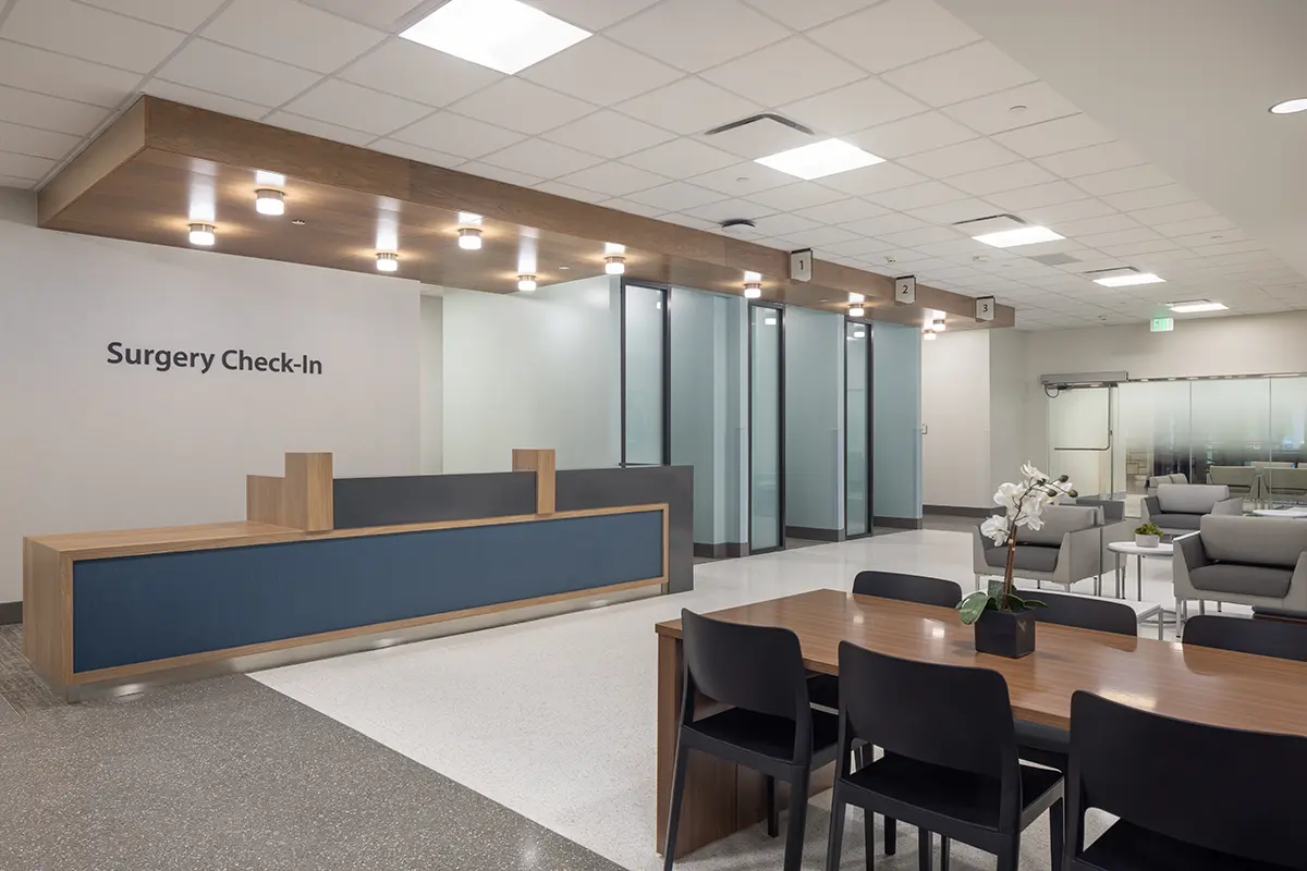 Modern surgery check-in area with sleek design, featuring a blue receptionist desk, frosted glass partitions, and comfortable seating. Bright, calm ambiance.