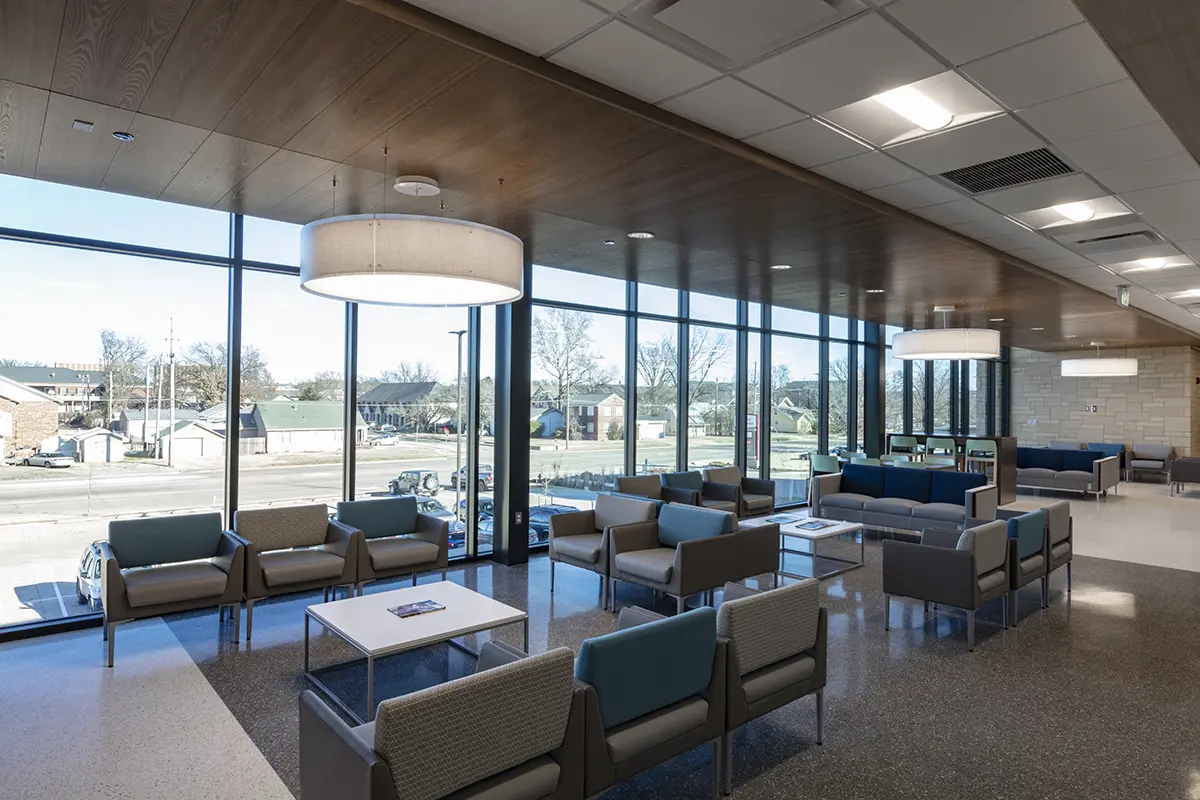 Spacious waiting room with modern furniture, large windows offering a view of a suburban street. Bright, calm ambiance with natural and overhead light.