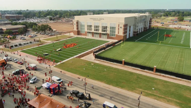 Aerial view of a sports complex with two football fields surrounded by a crowd of people in red clothing. The atmosphere is lively and festive.