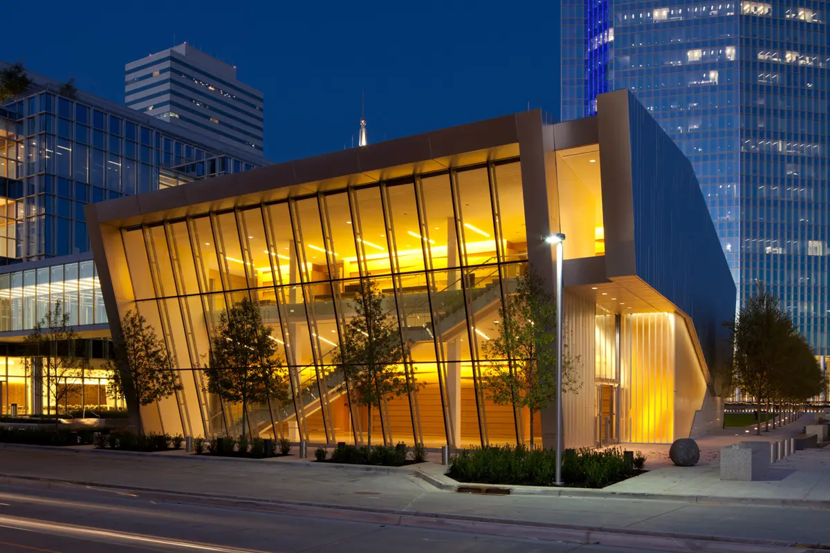 Modern building glowing with warm yellow lights against a nighttime cityscape. Glass facade and angular design create a striking, inviting appearance.
