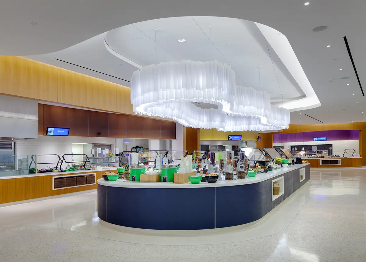 Modern cafeteria with sleek counters, bright lighting, and colorful decor. Large, white, cloud-like ceiling feature creates a welcoming atmosphere.