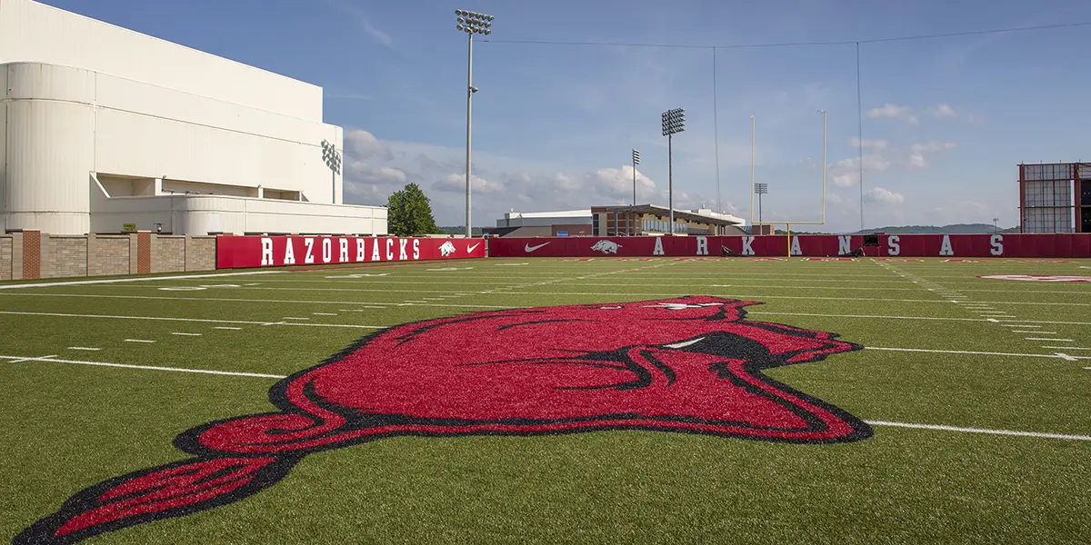 Modern lecture hall with tiered gray seating and red accents, featuring a large projection screen, red walls, and a boar logo on the carpet.