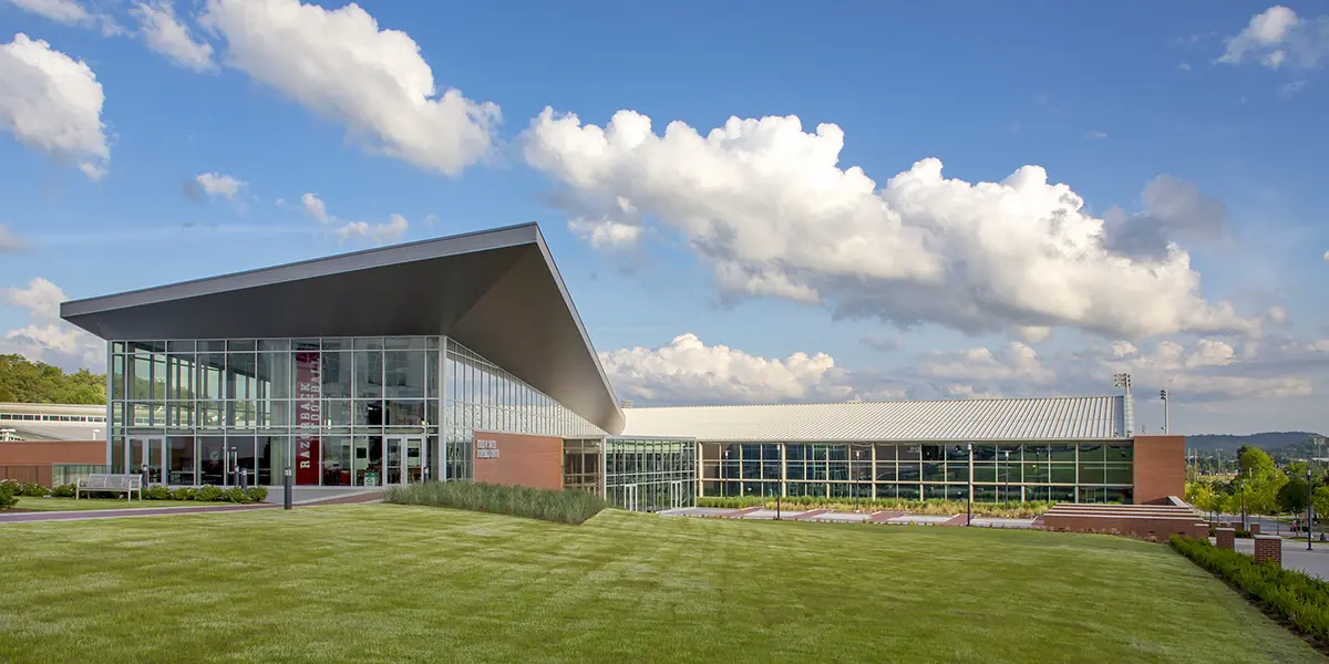 Modern lecture hall with tiered gray seating and red accents, featuring a large projection screen, red walls, and a boar logo on the carpet.