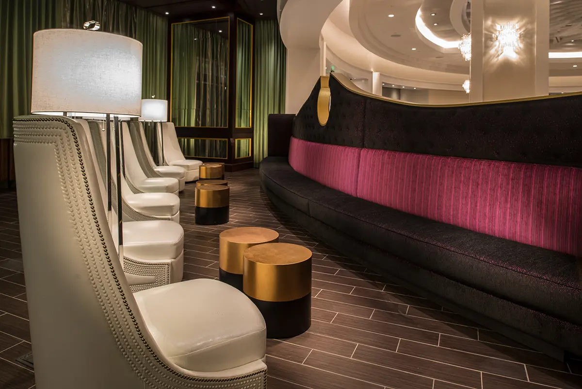Elegant hotel lobby with white chairs, tall lamps, and round wooden tables on a tiled floor. A curved couch with pink and black upholstery adds sophistication.