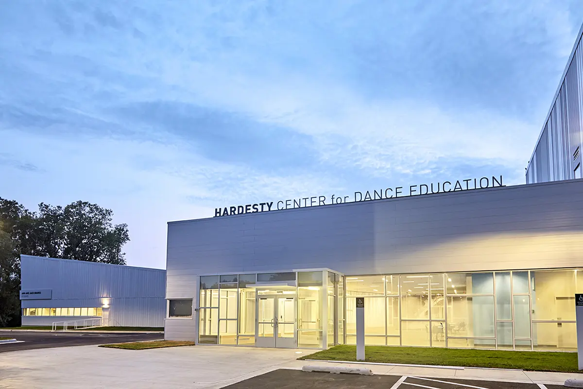 Modern building labeled "Hardesty Center for Dance Education" under a serene blue sky. Glass entrances and clean architecture convey a welcoming atmosphere.