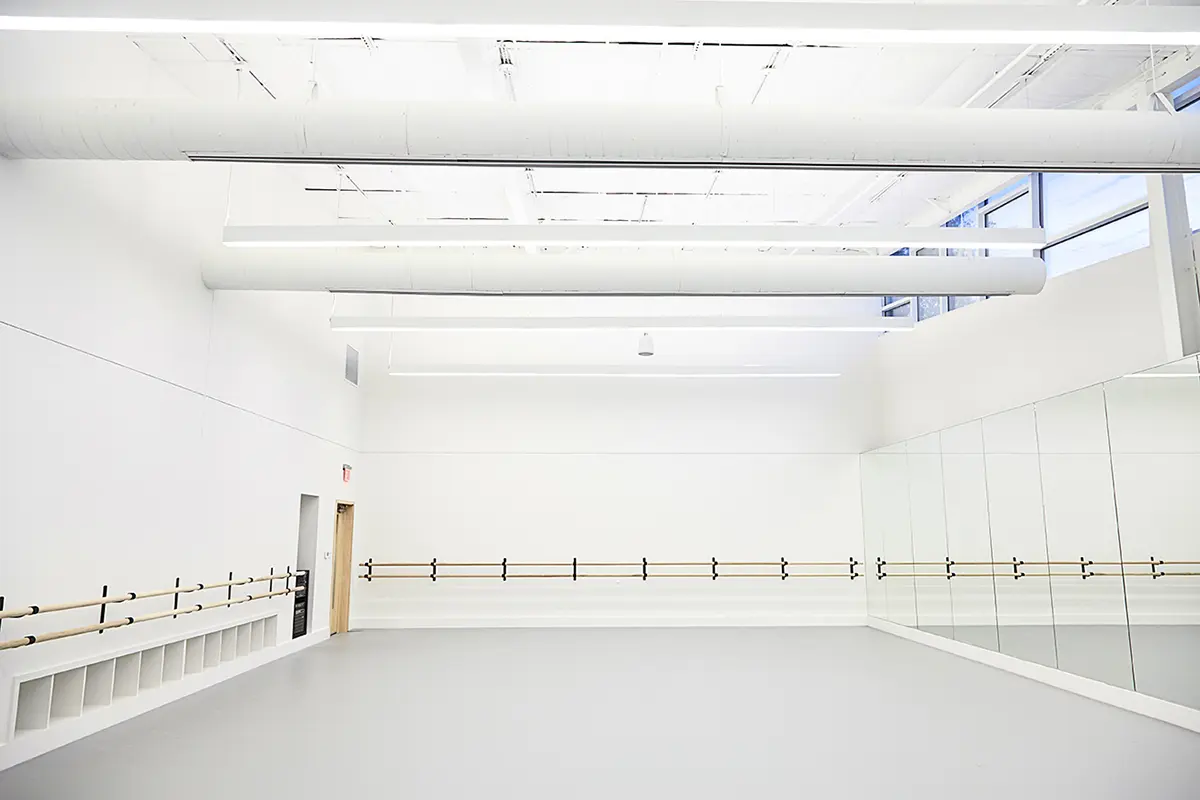 Bright, spacious dance studio with mirrored walls and wooden ballet barres. White ceiling and floor create a clean, minimalist, and serene atmosphere.