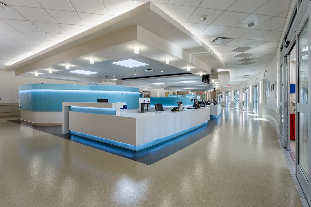 Moderna zona de recepción de un hospital con un elegante diseño en blanco y azul. Mostrador curvo, iluminación brillante y un ambiente tranquilo y estéril. Pasillos vacíos que se extienden hacia el exterior.