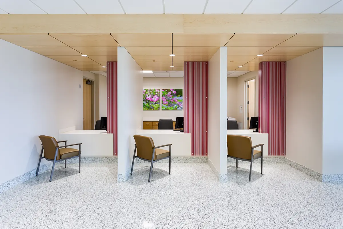 Moderna sala de espera con tres mostradores de recepción separados por divisores blancos, sillas acolchadas y detalles en rayas rosas. Un ambiente luminoso y sereno.