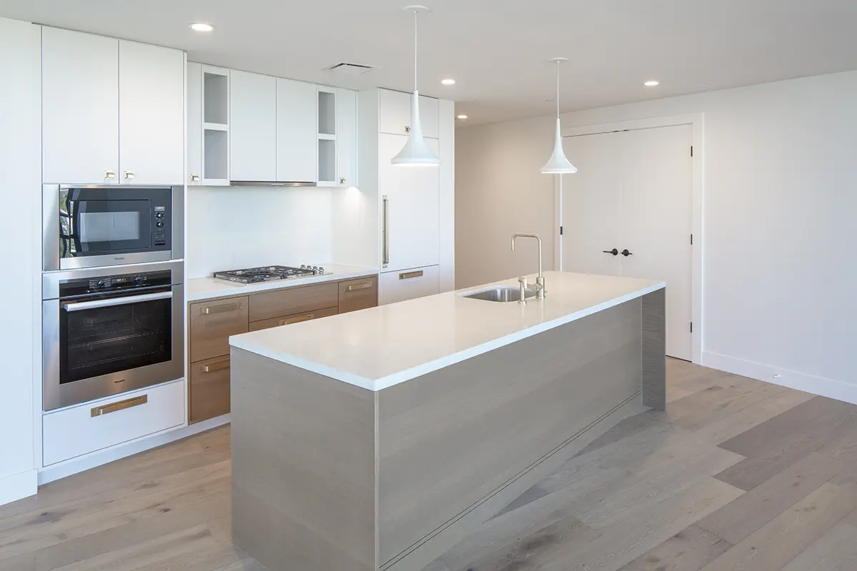 Modern kitchen with light wood flooring, white cabinets, and stainless steel appliances. Central island with sink, pendant lights, and a minimalistic feel.