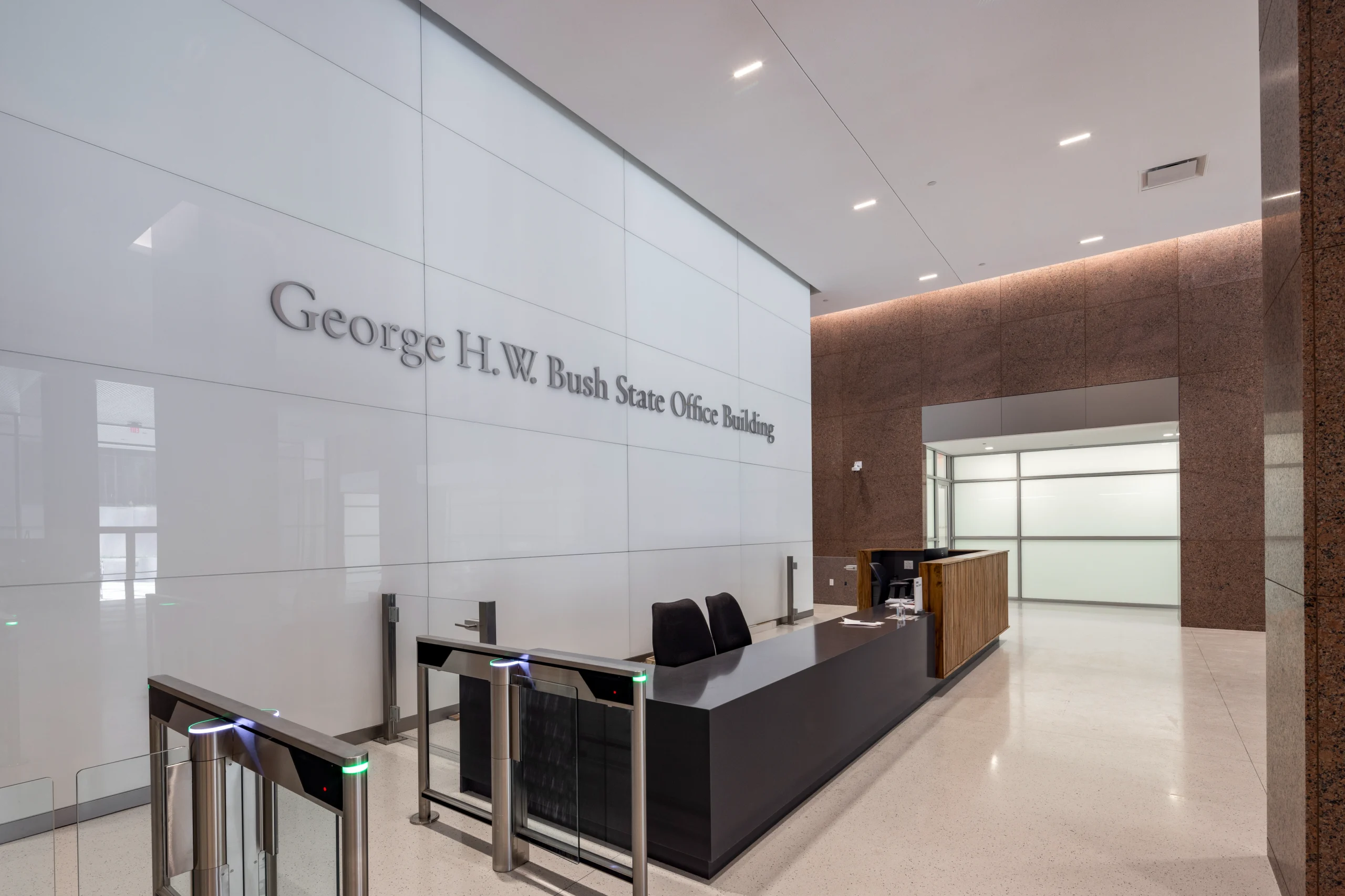 Modern lobby of the George H.W. Bush State Office Building with sleek reception desk, turnstiles, and minimalist design, conveying a professional tone.