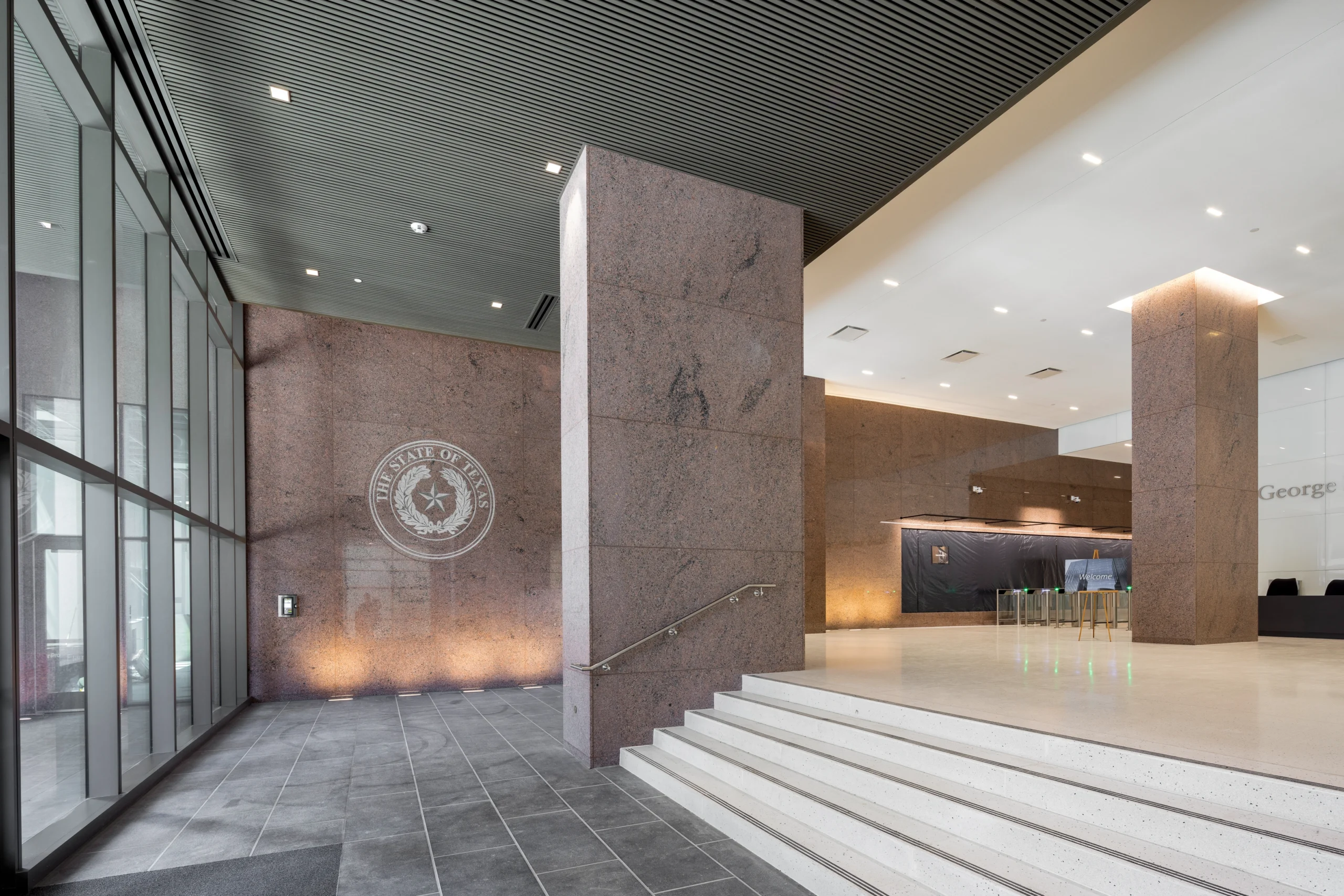 Modern office lobby with tall granite columns, polished floors, and an emblem on the wall. Soft lighting and high ceilings create an elegant atmosphere.