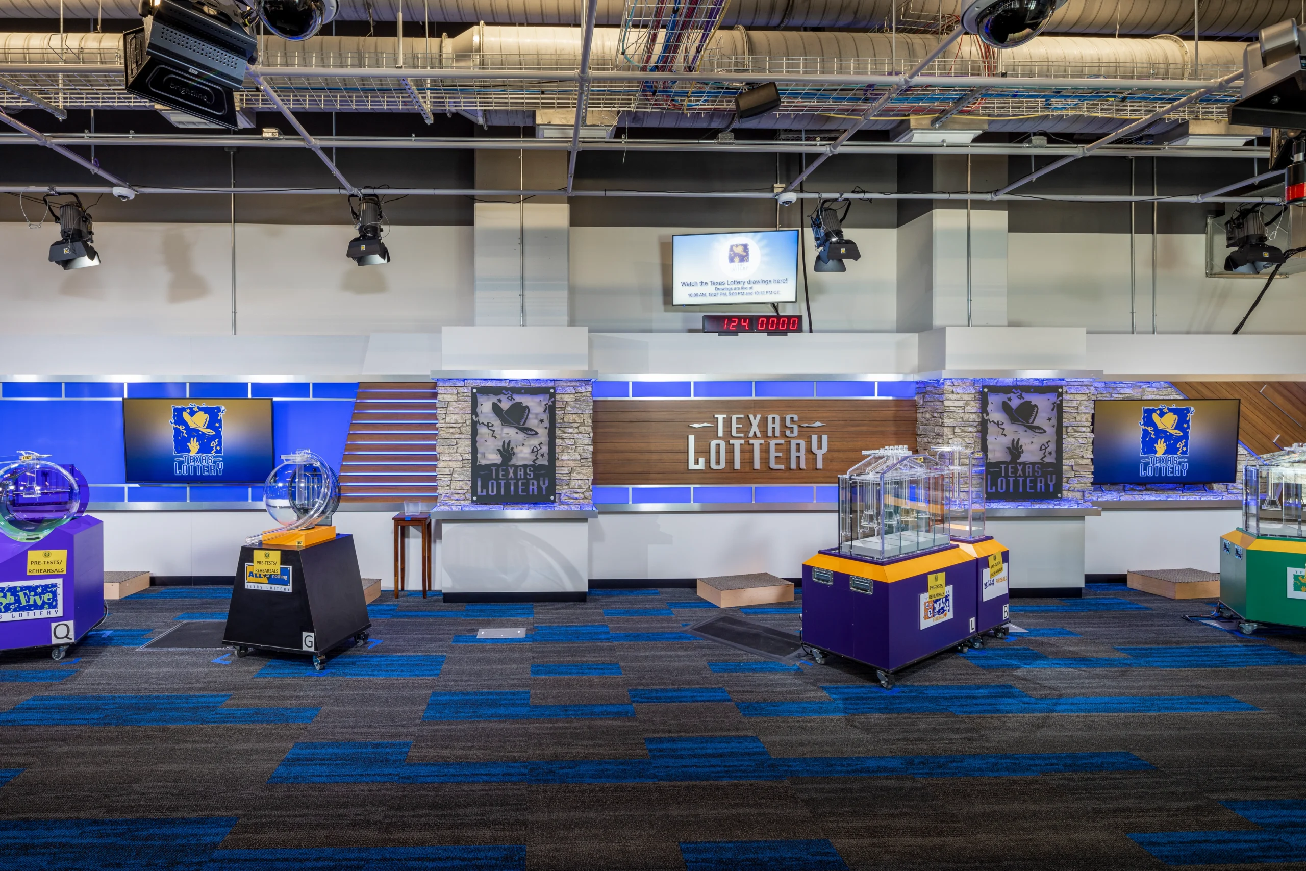 Texas Lottery studio with blue accents, showing lottery machines on colorful tables. The bright room is organized and ready for a live draw.