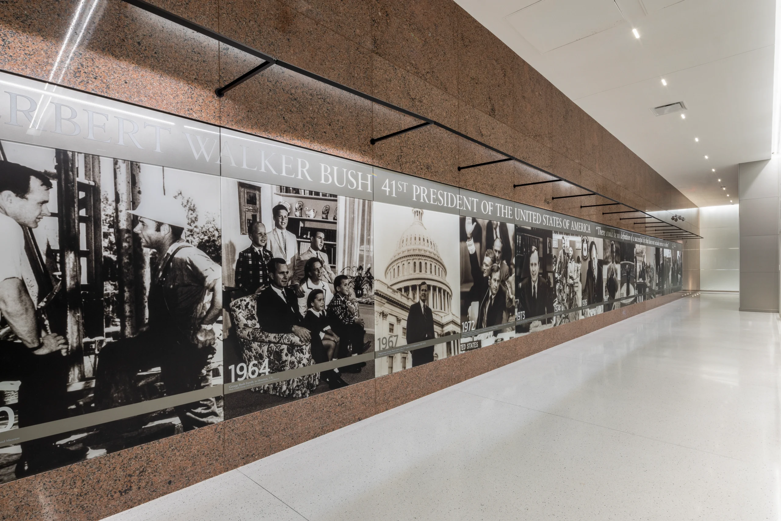Hallway mural displaying a timeline of monochrome images depicting milestones of George H.W. Bush's life, with a solemn and historical tone.