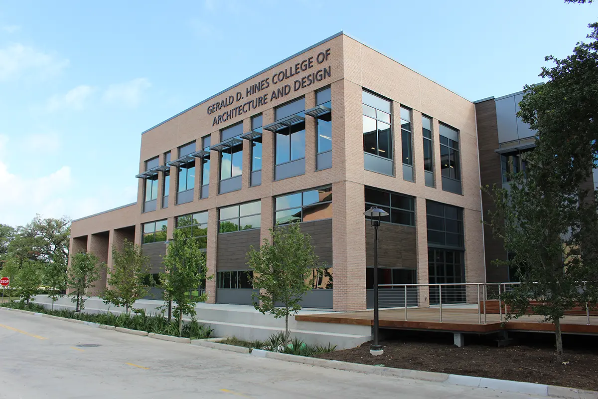 Modern brick building of Gerald D. Hines College of Architecture and Design. Large windows, trees in foreground, clear sky, bright and inviting.