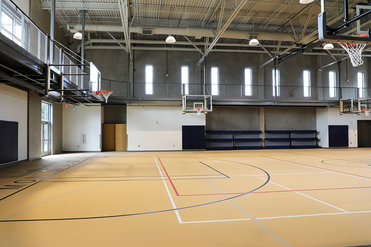 Spacious indoor basketball court with hardwood flooring, multiple hoops, and high windows. Bright, airy atmosphere with modern design elements.