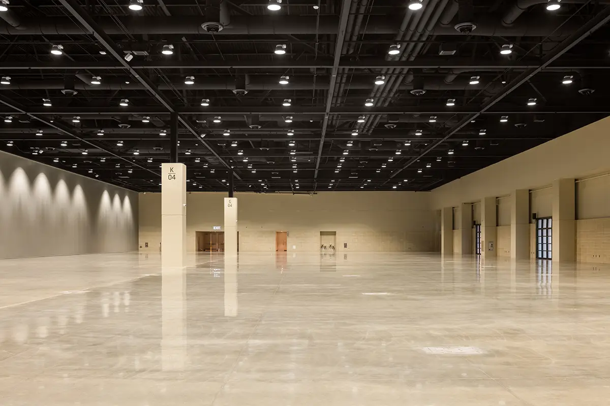 Spacious, empty convention hall with polished floors and high ceilings. Bright overhead lights reflect on the glossy surface, creating a neutral, clean ambiance.