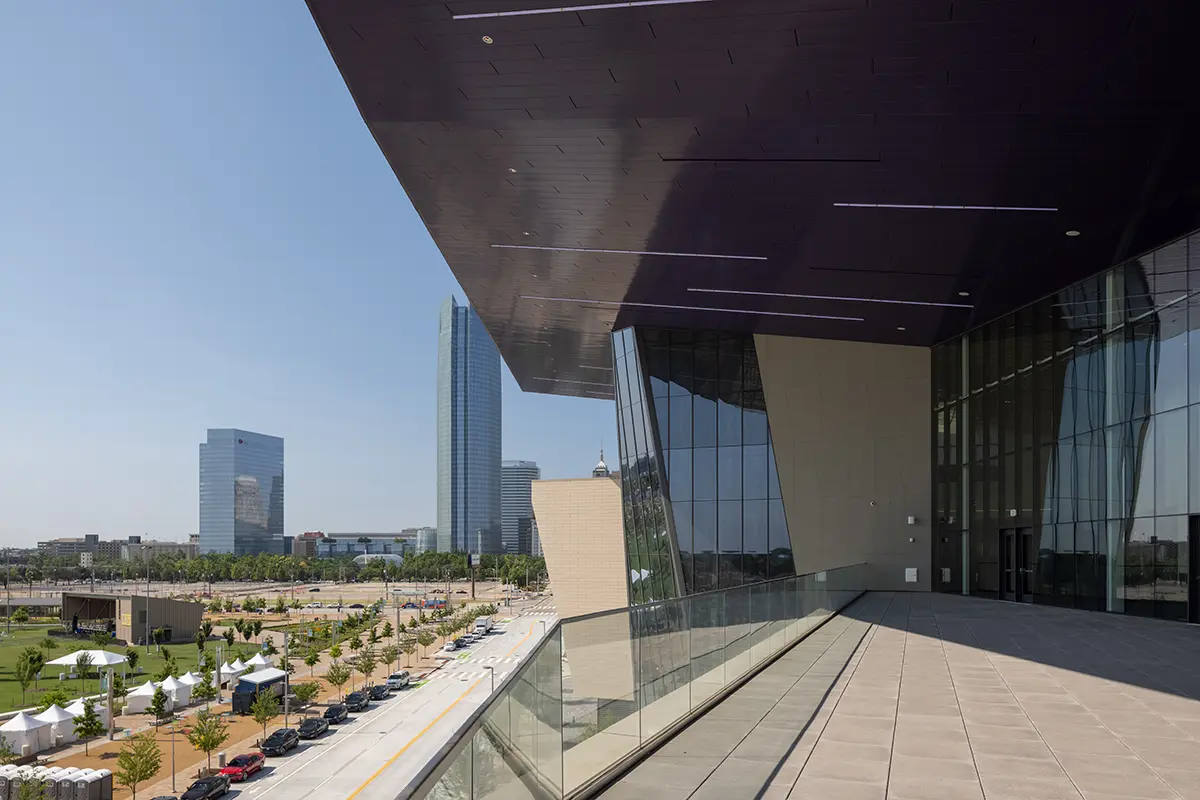 Modern cityscape with tall glass buildings under a vast blue sky. A large, sleek balcony with reflective surfaces offers a panoramic view, creating a serene, urban atmosphere.