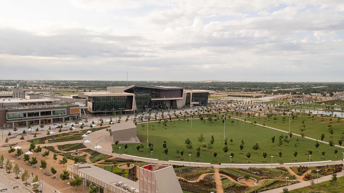 Aerial view of a modern university campus with expansive green lawns, landscaped pathways, and contemporary glass buildings under a partly cloudy sky.