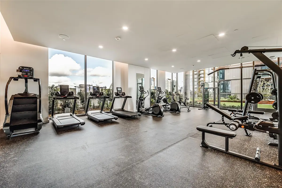 Modern gym with large windows showcasing city views. Features treadmills, exercise bikes, and weight machines. Bright, spacious, and inviting atmosphere.