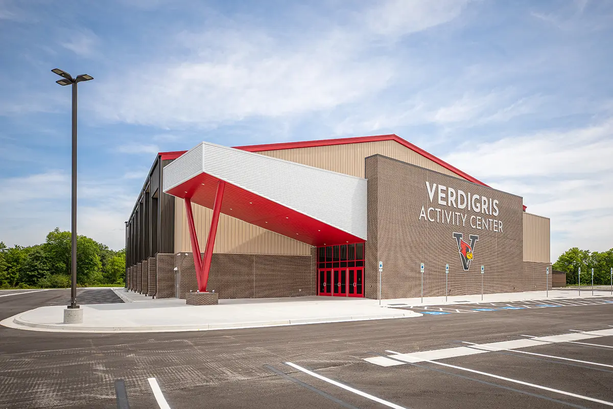 A modern building labeled "Verdigris Activity Center" features a geometric red and white entrance. Clear skies and a large parking lot surround it.