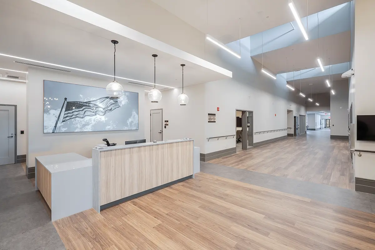 Spacious, modern lobby with a wooden reception desk and elegant globe lights. Above, there's a large American flag art piece. The atmosphere is serene.