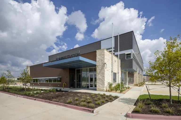 Modern two-story building labeled "Administration" with stone cladding and glass entrance under a blue steel awning, set against a bright blue sky.