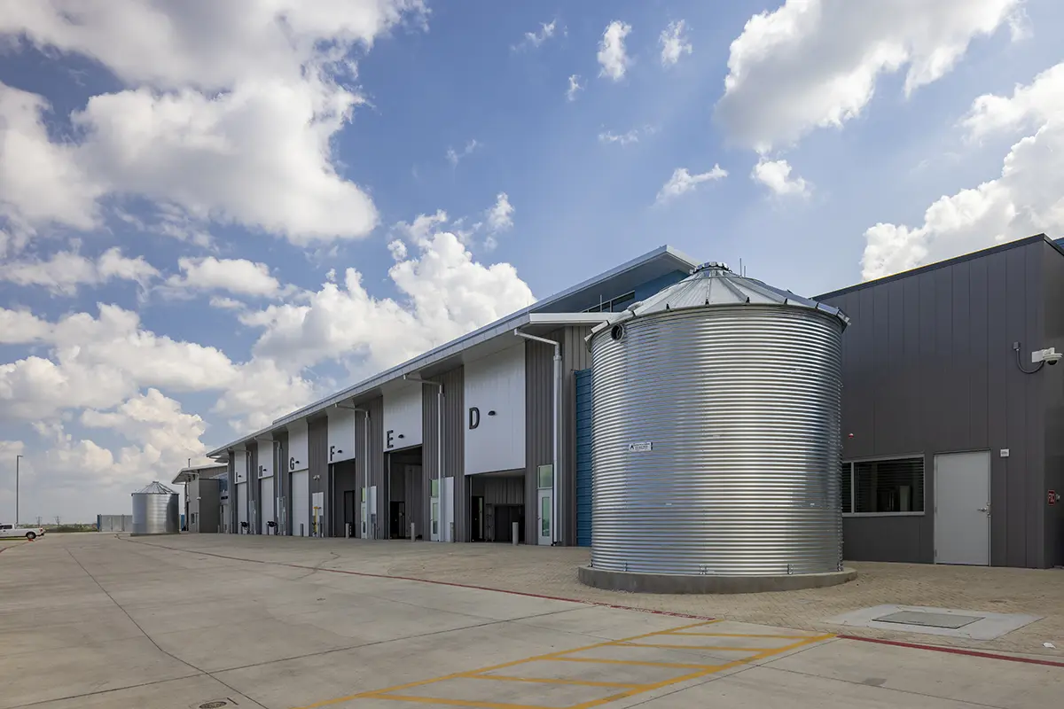 Modern industrial facility with large metal silos and numbered loading bays under a blue sky with scattered clouds, conveying a sense of scale and efficiency.