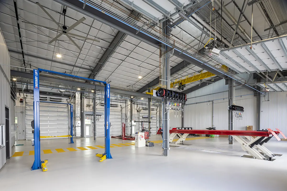 Bright, spacious auto repair shop with high ceilings, blue lifts, red car platform, overhead cranes, and organized equipment, conveying efficiency.