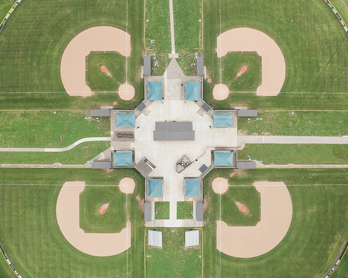 Aerial view of a park featuring five symmetrical, circular baseball fields with green grass. Central pavilion and paths connect the fields, creating a star-like pattern.
