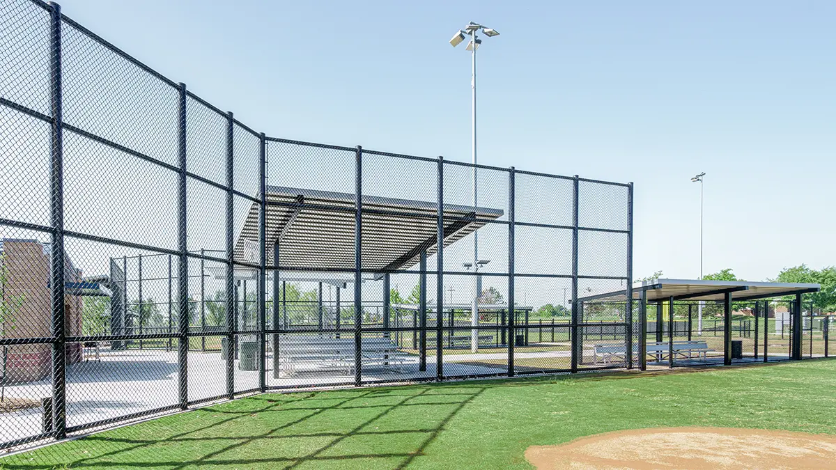 Outdoor baseball field with metal bleachers enclosed by a tall chain-link fence. Bright, clear sky lends a calm, open atmosphere to the scene.
