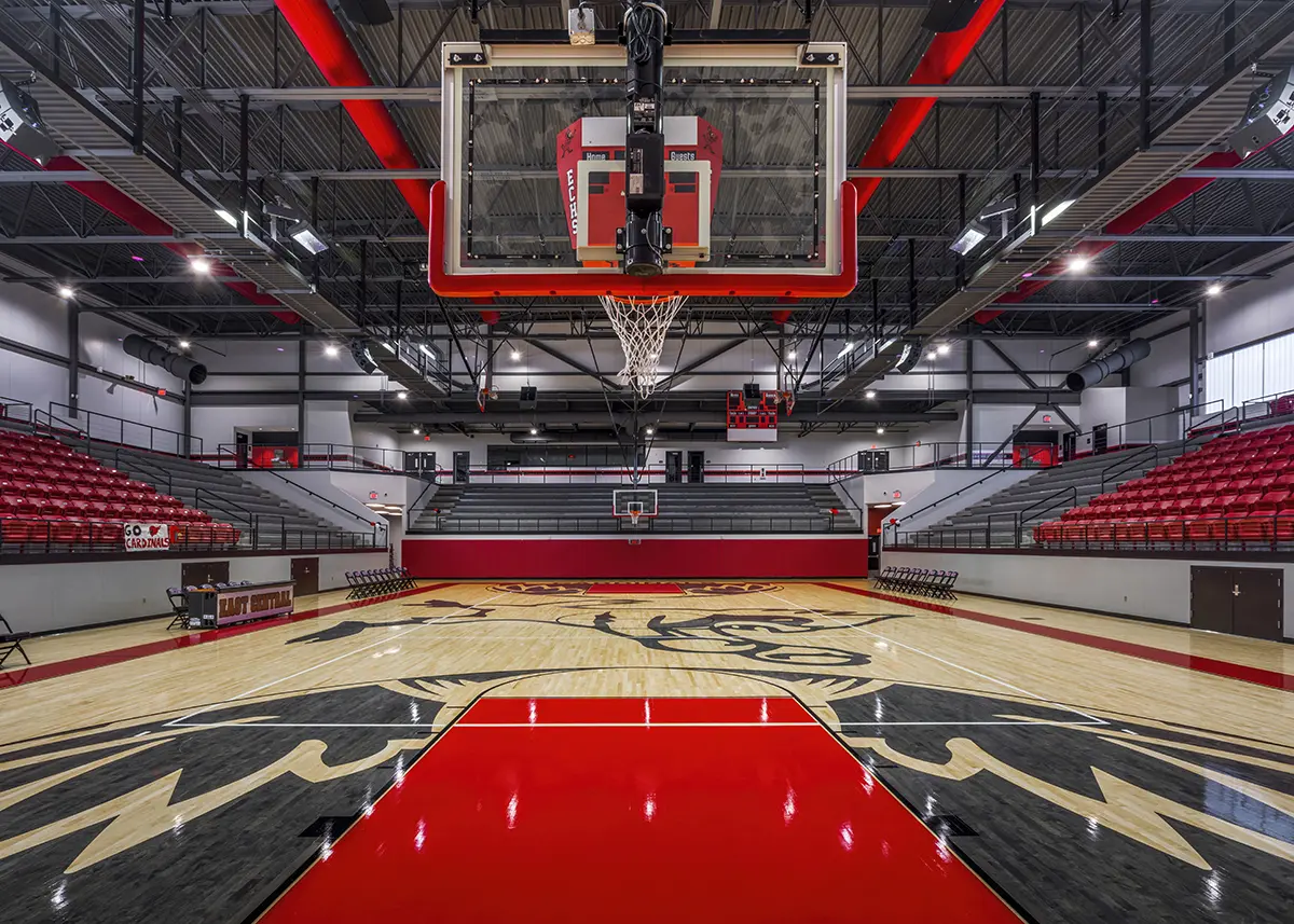Alt text: A spacious indoor basketball court with a red and wood color scheme, featuring red seats and a black eagle design on the floor, under bright lights.