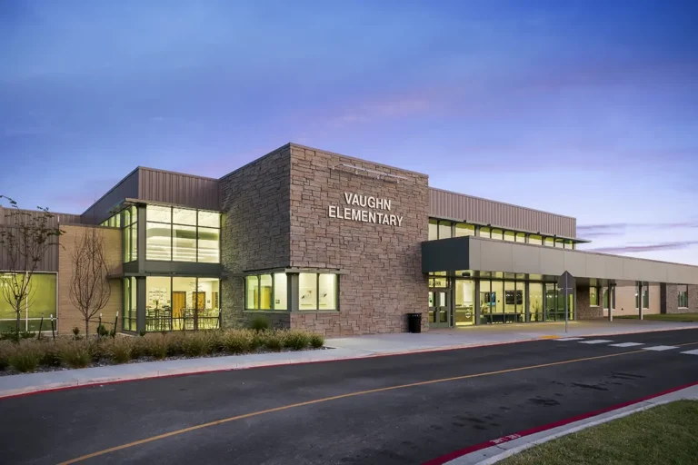 Modern elementary school building with large glass windows and stone facade, labeled "Vaughn Elementary." The sunset sky adds a calm tone.
