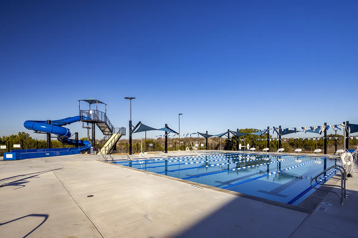 푸른 하늘 아래 슬라이드와 그늘이 있는 야외 수영장. 수영장은 비어 있어 고요하고 편안한 분위기를 자아낸다.