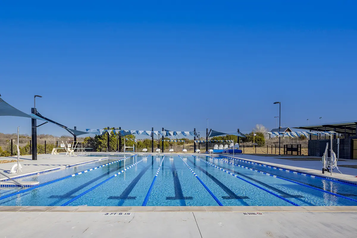 맑고 푸른 하늘 아래 위치한 야외 수영장으로, 레인 분할선, 그늘진 휴게 공간, 그리고 차분하고 편안한 분위기를 자랑합니다.